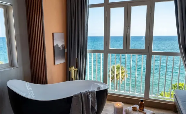 Black bathtub with a candle tray before windows on the sea and palms