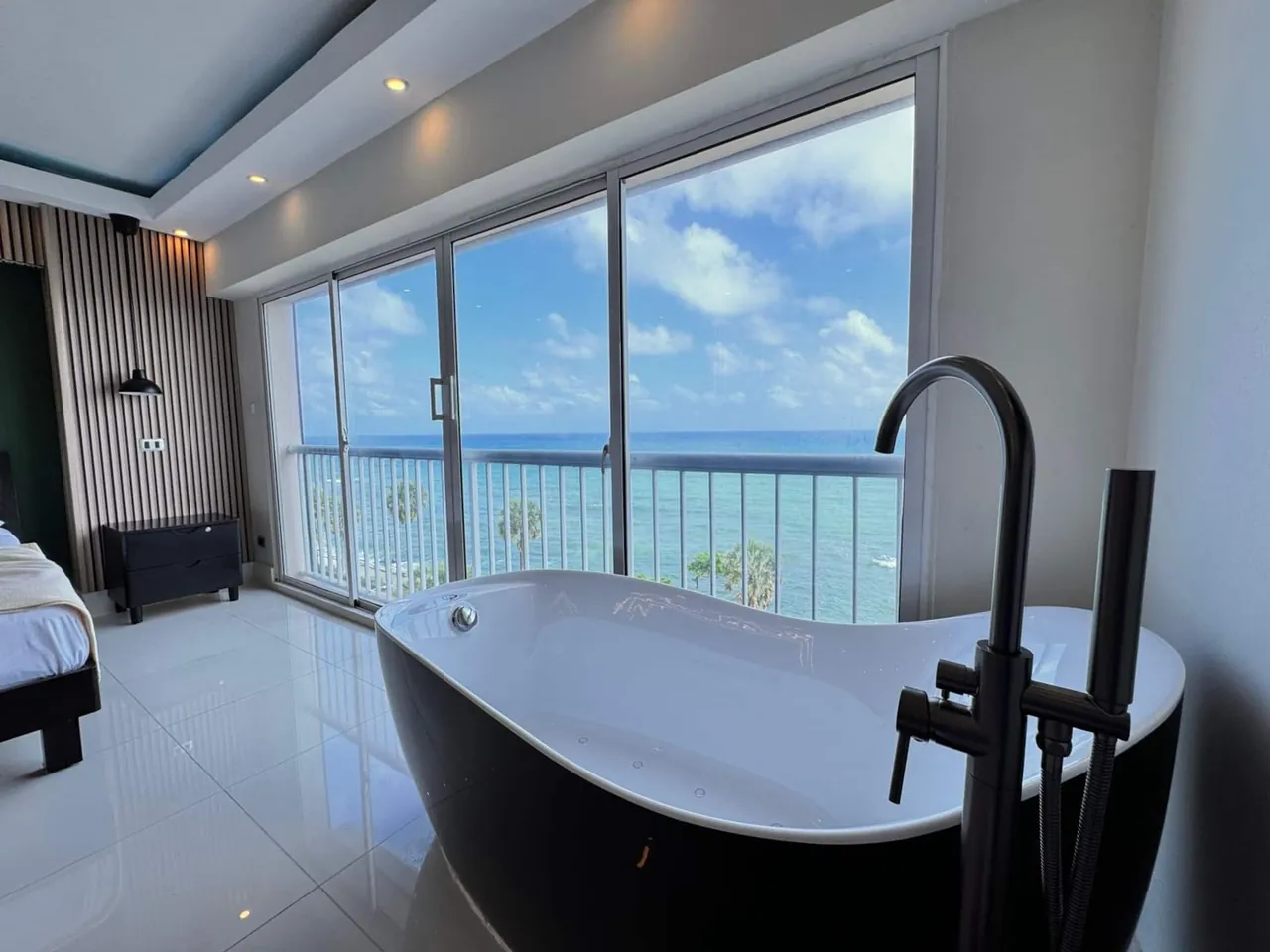 Black freestanding bathtub and floor faucet beside windows over the Caribbean