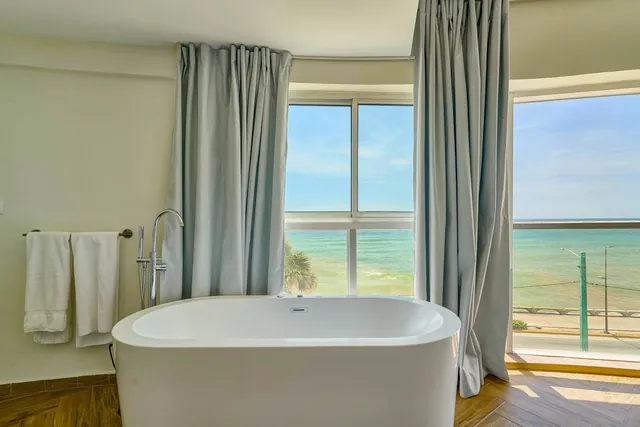 Loft bathtub framed by curtains and the sea