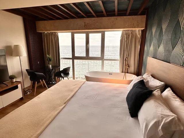 Studio with wood beams, a large bed and a tub at the window