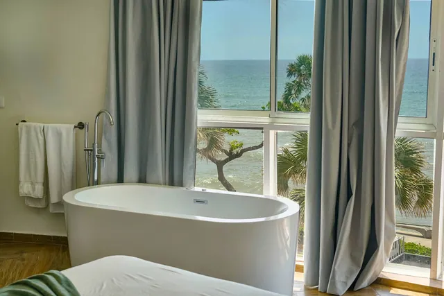 Freestanding bathtub between linen curtains with the sea beyond