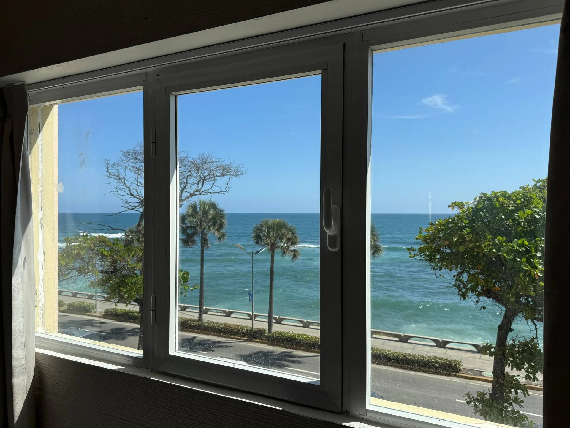 Floor-to-ceiling window framing the Malecón, palms and the sea