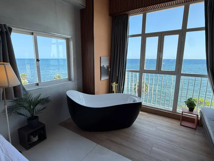 Black bathtub in a loft with the blue sea through tall windows