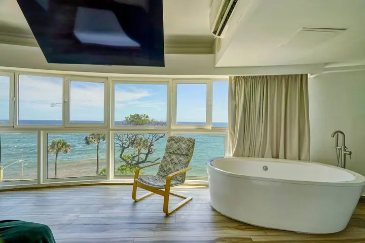 Oval bathtub and a reading chair facing a wide panorama of the sea