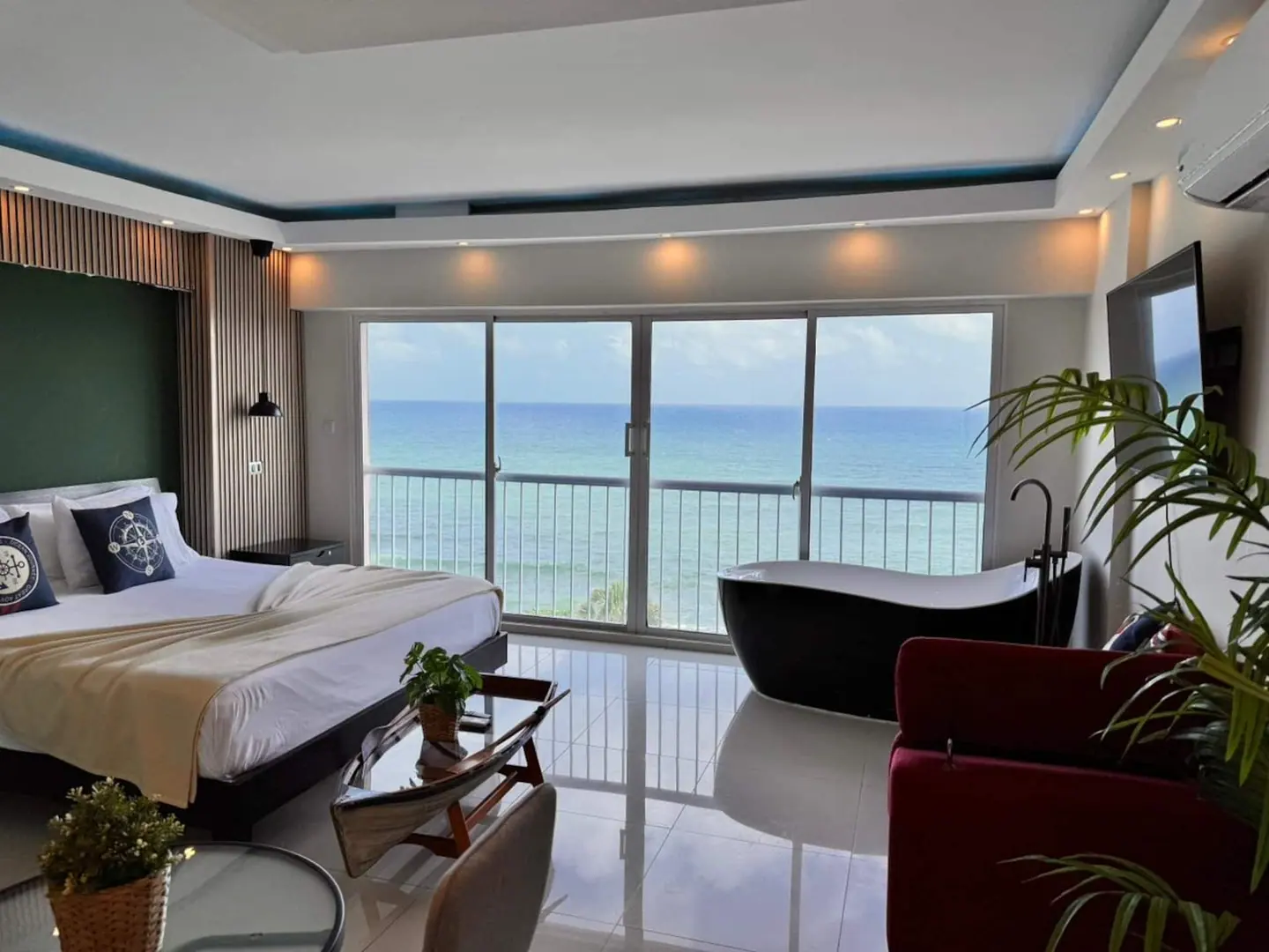Studio with a black freestanding bathtub, king bed and a wall of windows on the sea