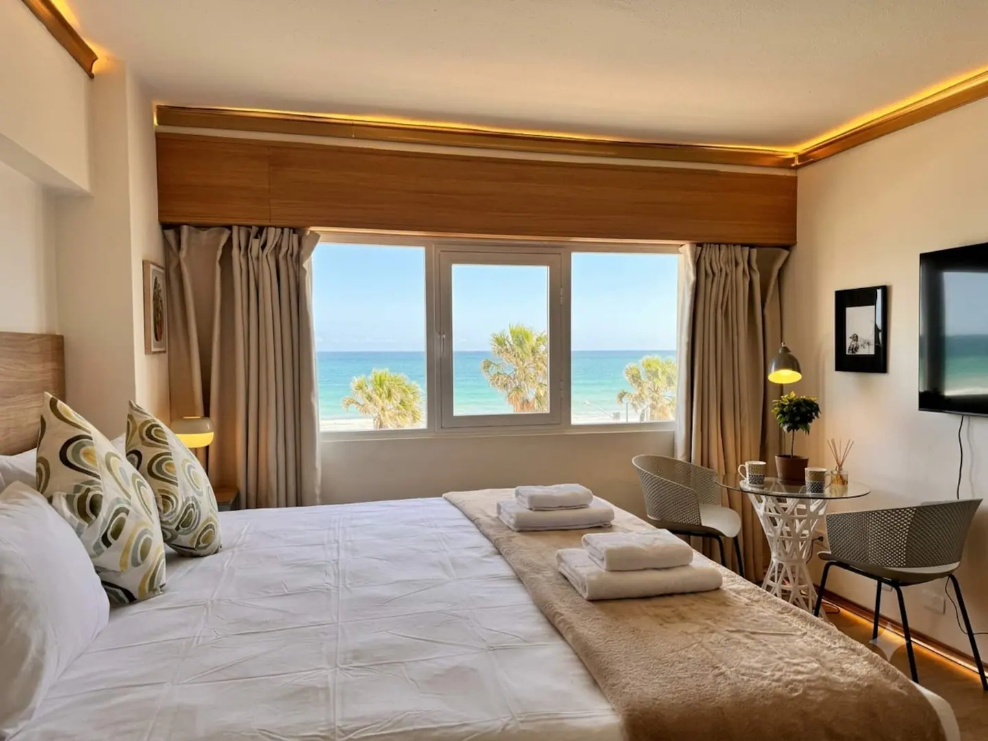 Bedroom with patterned pillows and palms and sea in the window