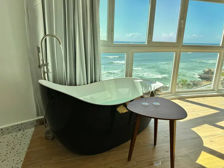 Black bathtub and side table in a corner of wraparound sea windows