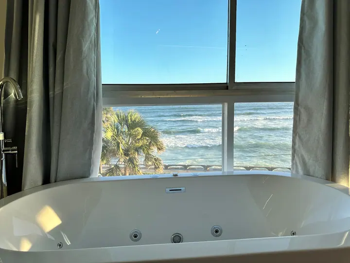 Jetted tub under a window with palms and surf below