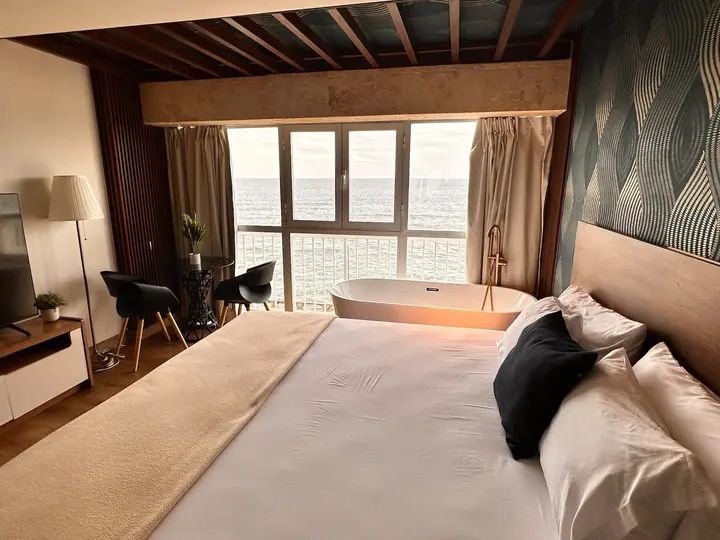 Studio with wood beams, a large bed and a tub at the window