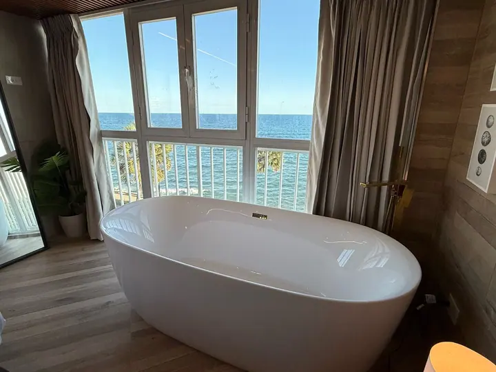 Freestanding bathtub framed by curtains and a blue sea