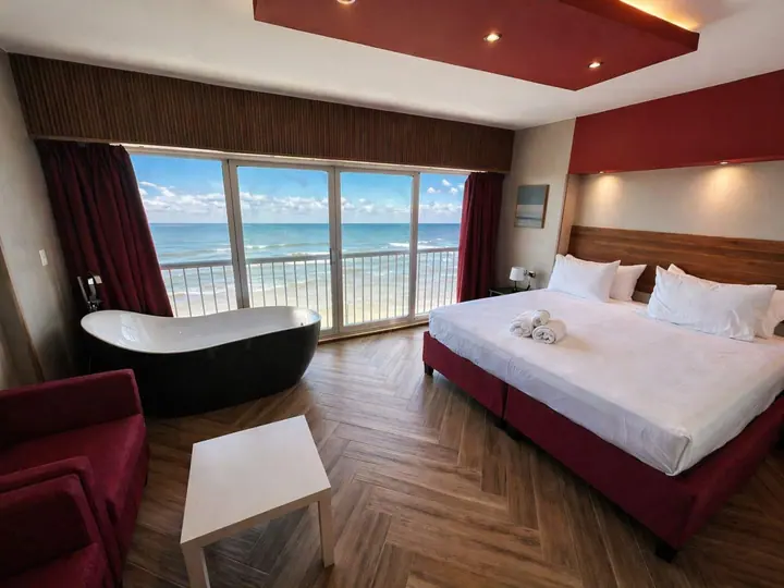 Studio with a black bathtub, red armchair and a king bed by the sea