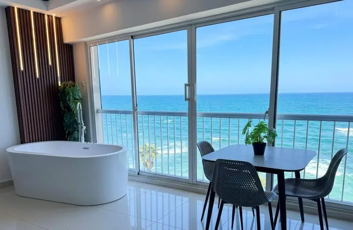 Bathtub and a small dining table by glass doors on the sea